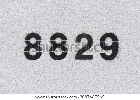 Black Number 8829 on the white wall. Spray paint. Number eight thousand eight hundred and twenty nine.