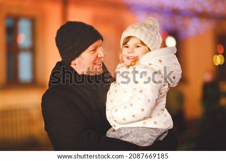 Little preschool girl sitting on shoulder of father on Christmas market in Germany. Happy toddler child and man walking on the streets of German festive city. Family, bonding, love. Family xmas time