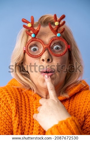 Senior woman holding thumbs up and showing shocked expression wearing Xmas glasses