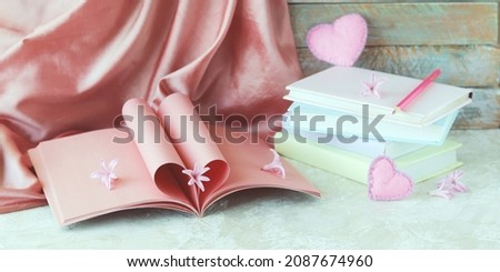 Pink heart-shaped notebook pages are decorated with fresh flowers, on a background of natural silk fabric, romantic jewelry and stacks of books, emotion of love, Valentine's Day, congratulations, gift