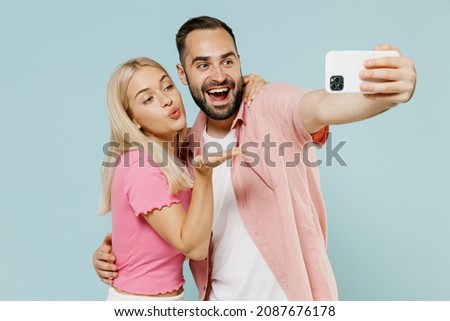 Young fun couple two friends family man woman in casual clothes doing selfie shot on mobile cell phone post photo blow air kiss together isolated on pastel plain light blue background studio portrait