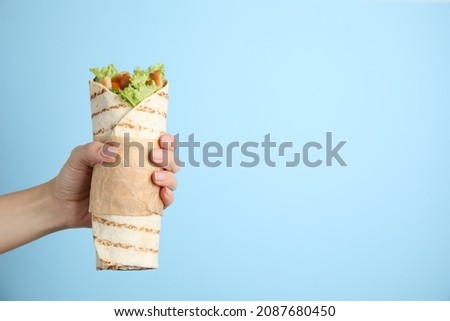 Woman holding delicious chicken shawarma on light blue background, closeup. Space for text Royalty-Free Stock Photo #2087680450