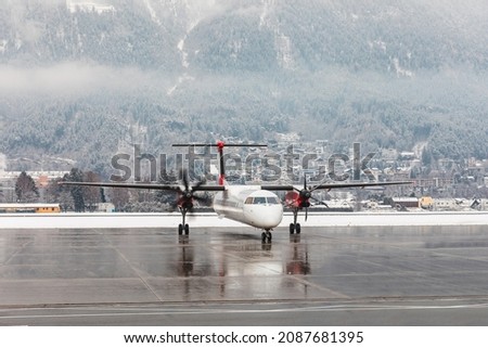 Airplane starting engines with snow winter background - Small regional jet getting ready to depart from Innsbruck airport on a winter day - Travel and transportation concepts