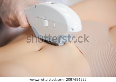 The procedure of laser hair removal of a young girl abdomen with modern tools by a professional specialist in the clinic