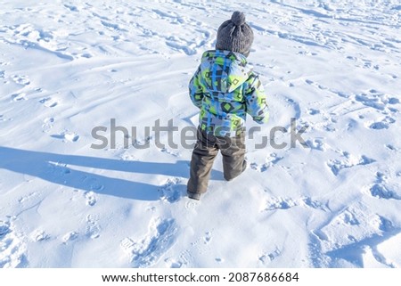 A child with a serious expression on his face in winter clothes jackets, pants, hat and boots in winter on the white snow on the street and in the park in nature plays winter fun.