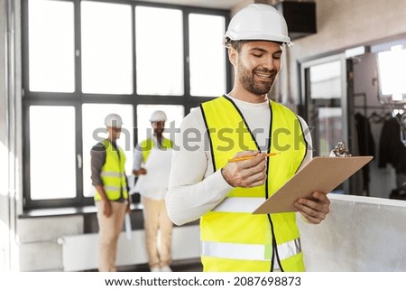 architecture, construction business and building concept - happy smiling male architect in helmet and safety west with clipboard working at office