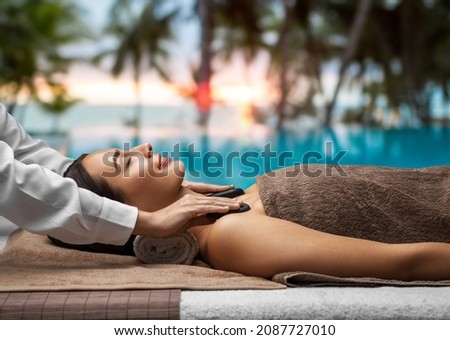 wellness, beauty and relaxation concept - beautiful young woman having hot stone massage at spa over tropical beach background in french polynesia Royalty-Free Stock Photo #2087727010