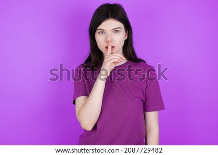 Caucasian woman wearing purple T-shirt isolated over studio background makes silence gesture, keeps finger over lips. Silence and secret concept.