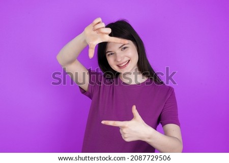 Caucasian woman wearing purple T-shirt isolated over studio background making finger frame with hands. Creativity and photography concept.