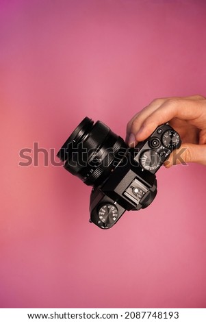 a man holding a mirrorless camera on a pink background top view. photographer takes pictures on camera. modern camera