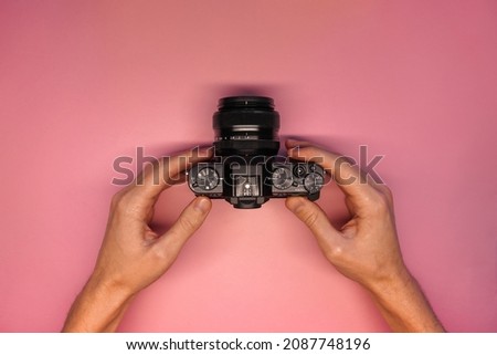 a man holding a mirrorless camera on a pink background top view. photographer takes pictures on camera. modern camera