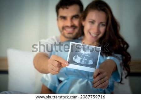 The happiness of a pregnant woman and her husband in the bedroom with the ultrasound film of the fetus that shows the results that the child is healthy