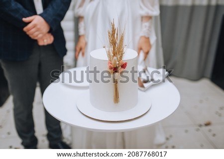 A beautiful white cake decorated with reeds stands on the table, against the backdrop of the newlyweds. Wedding photography.