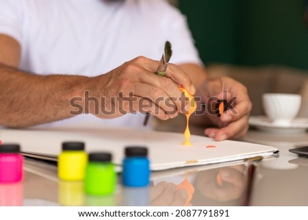 man in white t-shirt drinking coffee, practicing art therapy, pouring orange paint on blank canvas.