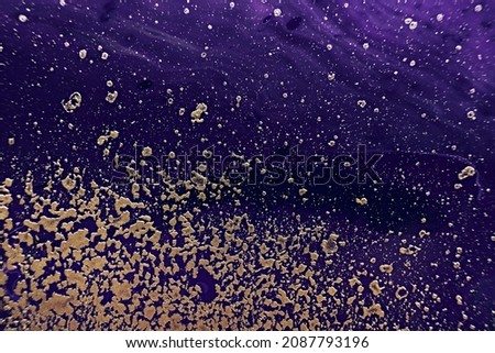 Fluid Art. Golden spray particles and purple waves on black background. Marble effect background or texture