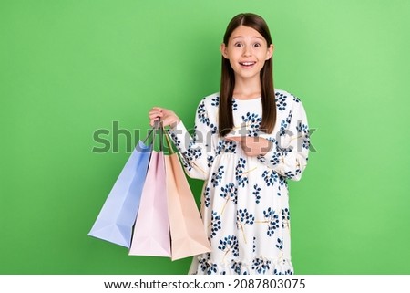 Look bargain. Shocked kid girl buyer shopaholic point shopping bag wear trendy clothes isolated over green color background