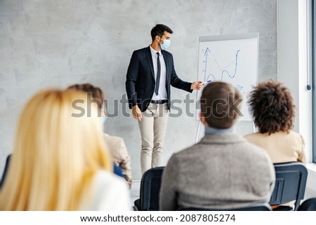 Economist presentation, seminar, and education. A young economist having speech, standing next to a chart board and pointing at it while the audience listening to his lecture.