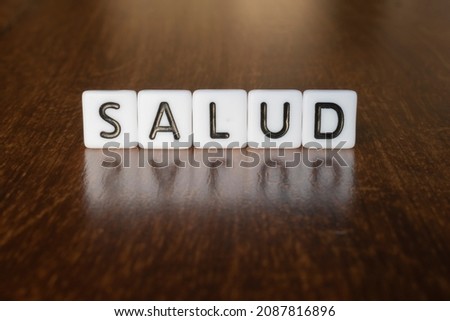 Health (Salud) word written on blocks. Word Health (Salud) isolated on wooden background with reflection