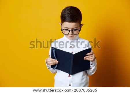 Portrait of a smiling kid wearing white shirt and glasses holding an open book