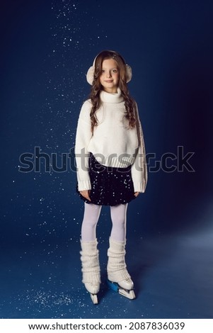 girl in a white sweater , skirt and warm winter headphones on figure skates in a studio on a blue wall in Christmas