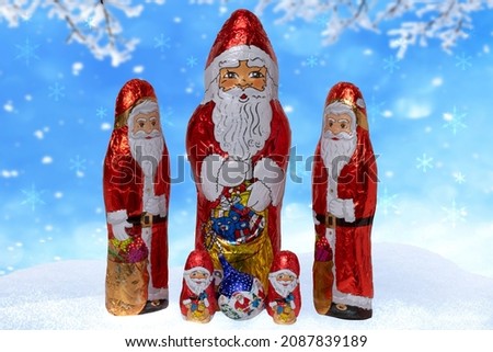 Christmas greeting card. Closeup of various cheerful wrapped chocolate Santa Claus over festive abstract blurred winter landscape. Xmas and New Year gift sweets. Macro.