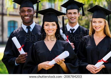 Feeling confident in their future. Four college graduates in graduation gowns standing close to each other and smiling