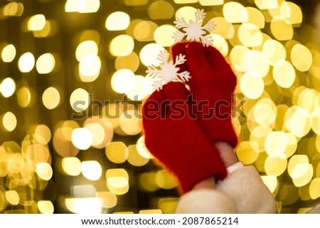 hands in red mittens ,close - up against the background of lights ,holding white snowflakes