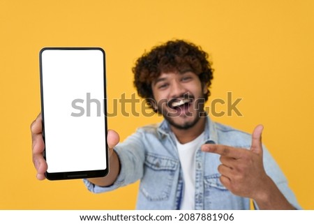 Happy excited young indian man showing smartphone pointing at big mockup white blank phone template screen isolated on yellow background presenting cellphone mobile offer application ads concept. Royalty-Free Stock Photo #2087881906