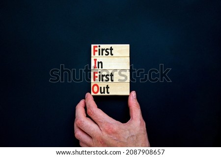 FIFO first in out symbol. Concept words FIFO first in first out on wooden blocks. Beautiful black table, black background. Businessman hand. Business FIFO first in and out concept. Copy space.