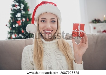 Photo portrait smiling woman sitting on sofa wearing white knitted sweater headwear keeping tiny present box Royalty-Free Stock Photo #2087925826