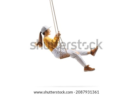 Full length profile shot of a young trendy female swinging on a wooden swing isolated on white background