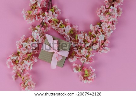 Top view of light cherry blossom flowers and a giftbox on a pink background for Mothers Day or Easter holiday concept