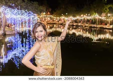 Thai girls wearing Thai costumes take pictures with colorful lights in the background as a night photo shoot, with a good mood smiling in the city of Siam of Thailand.