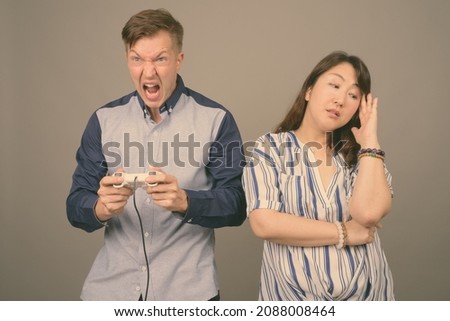 Studio shot of young handsome businessman and mature Asian businesswoman against gray background