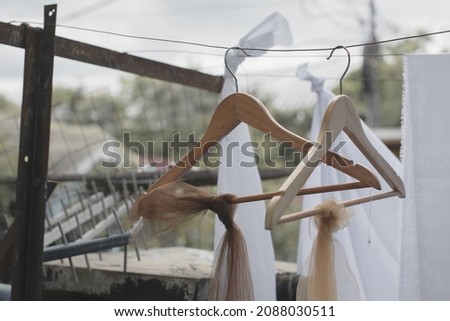 An image of two wooden clothes hangers hanging on a thin steel wires, that has a transparent fabrics tied on it.