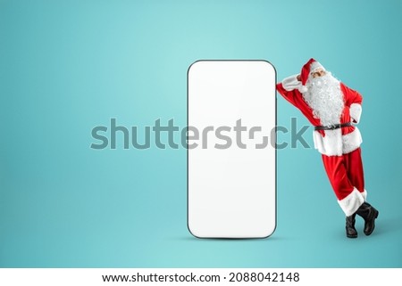 Smartphone mockup image, environment to showcase mobile app design, creative background. Smartphone for your advertising. Santa claus is standing next to a large smartphone. Christmas advertisement