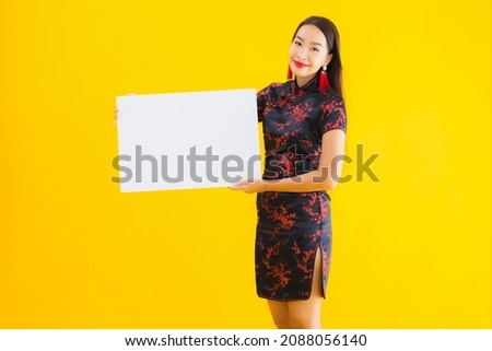 Portrait beautiful young asian woman wear chinese dress show white empty billboard for text in chinese new year concept on yellow isolated background