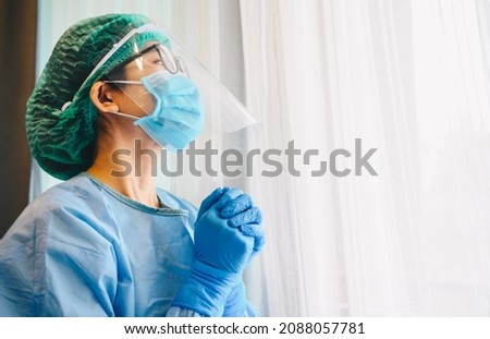 Healthcare worker praying for god blessing while wearing safety equipment for working in hospital during coivd-19 pandemic. Conceptual of woman praying for god to help everythings will be better. Royalty-Free Stock Photo #2088057781