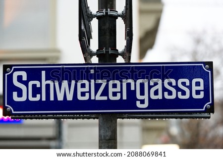 Road sign with text Schweizergasse (German, translation is Swiss alley)  at famous shopping mile Bahnhofstrasse at City of Zürich on a rainy day. Photo taken December 8th, 2021, Zurich, Switzerland.