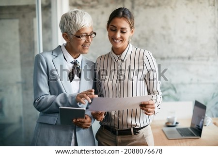 Happy senior CEO using touchpad while going through business reports with her young colleague in the office. Royalty-Free Stock Photo #2088076678