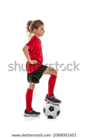 Portrait of girl, child in red uniform posing with football ball isolated over white background. Concept of action, sportive lifestyle, team game, health, energy, vitality. Copy space for ad