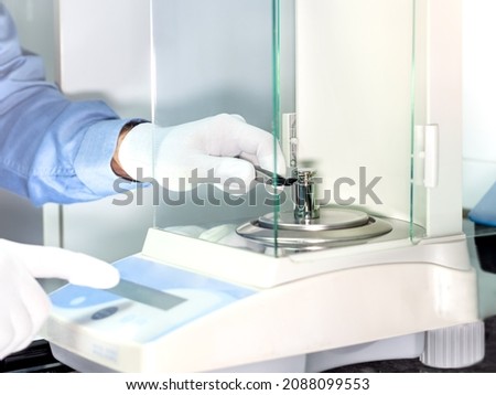 A operator's hand is holding steel calibration weight to place on the analytical balance. Concept of quality control in a laboratory. Royalty-Free Stock Photo #2088099553