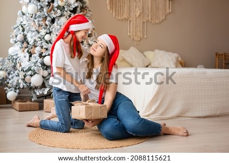 Sisters celebrate winter holidays. Girls exchange Christmas gifts near Christmas tree. Happy among New Year's decor. High quality photo