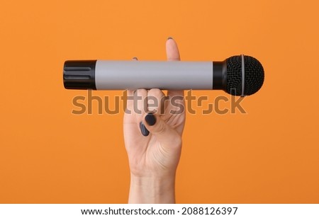 Female hand with modern microphone on color background