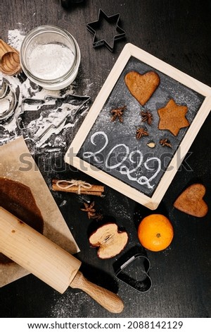 Baking Christmas gingerbread cookies on a dark wooden table. Preparing for baking. Winter holidays. 2022 New Year sign. Top view. 