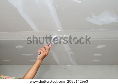 Construction worker plastering gypsum board or plasterboard panels wall with trowel. Home interior drywall works, renovation or construction Royalty-Free Stock Photo #2088142663