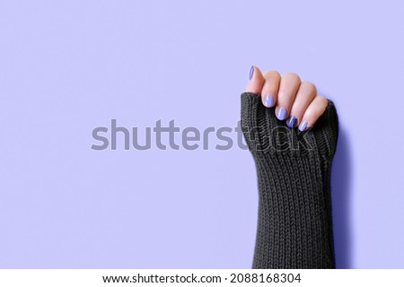 Detail of womans hand wearing grey sweater with trendy colors violet manicure nails on purple background