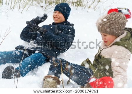 a girl and a boy are playing snowballs outside, beautiful winter weather and white snow around