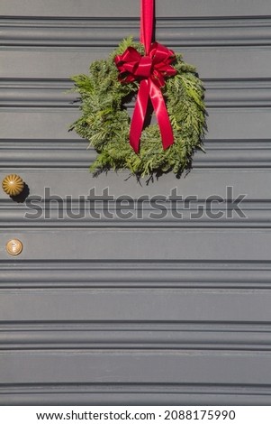 Decorative Advent wreath bonded with different conifer branches as fir, pine or spruce and fixed at a front door with a red fabric ribbon