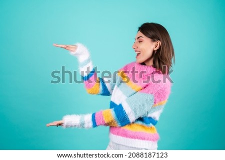 A young woman in a bright multicolored sweater on a blue background shows with her hands a large size, huge discounts, holds an empty space between her palms
